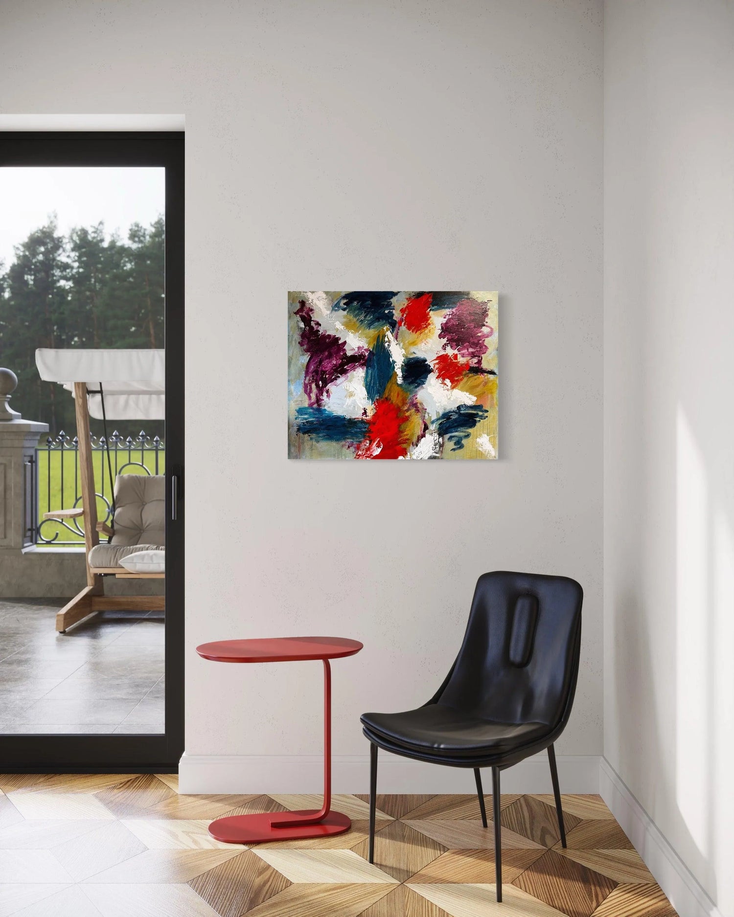 An abstract painting on the wall in the corner of a room, underneath it is a black chair and deep red metal side table. The floor is wooden, patterned not parquet. To the left of the photograph is a floor to ceiling window through which can be seen a veranda and a swinging chair with a canopy. A lawn and trees beyond.